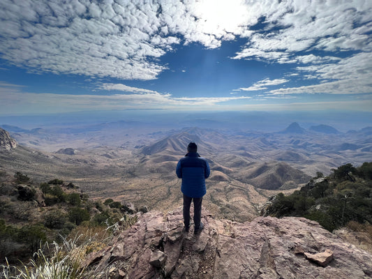 Hiker standing at the South Rim in Big Bend National Park overlooking the vast Chihuahuan Desert and distant mountains.